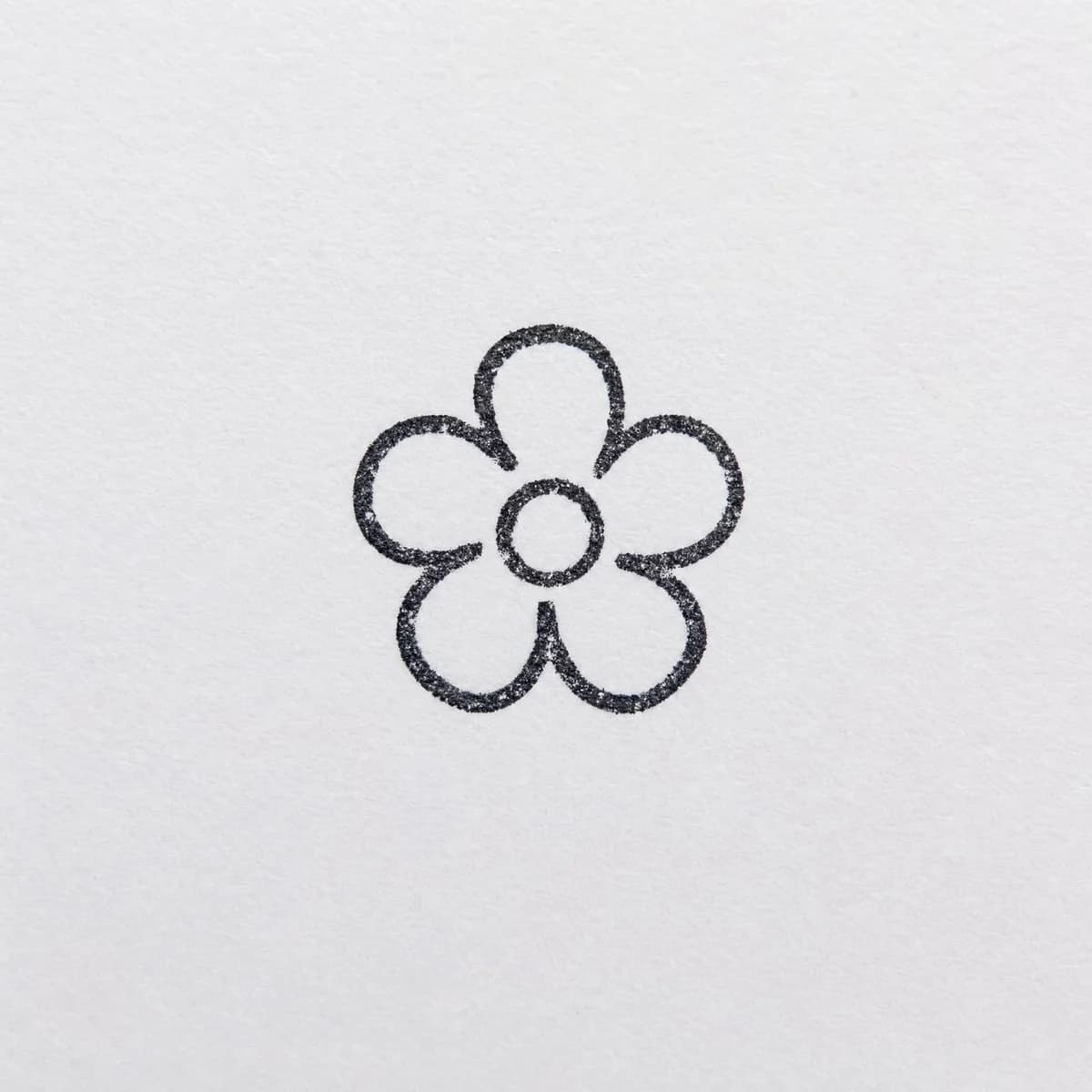 Petit logo de fleur sans cadre : exemple d’empreinte à l’encre noire sur papier blanc